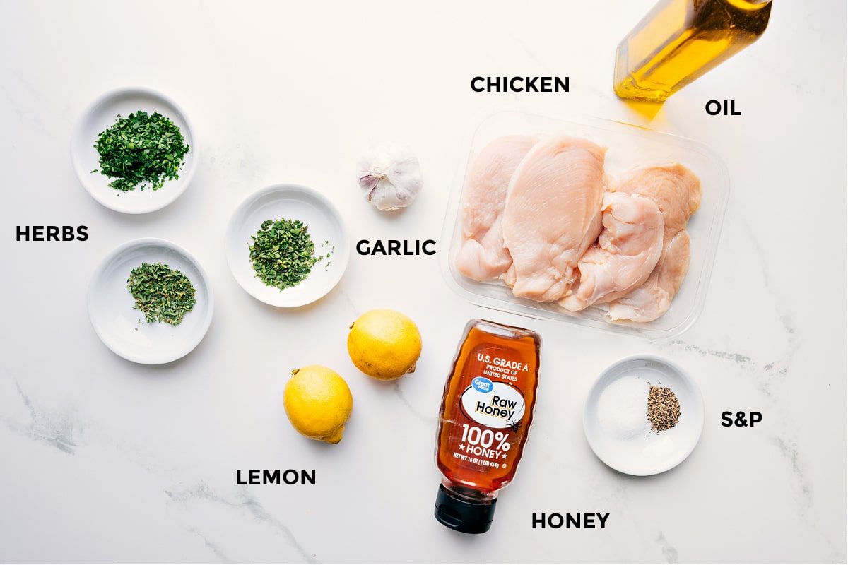 All the ingredients in this recipe prepped out for straightforward assembly including the herbs, lemon, garlic, chicken, honey, and oil.