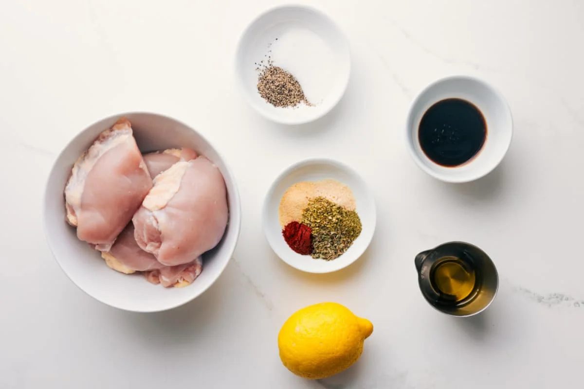 All the ingredients in this recipe prepped out for straightforward assembly including the chicken, seasonings, balsamic vinegar, lemon, and olive oil.