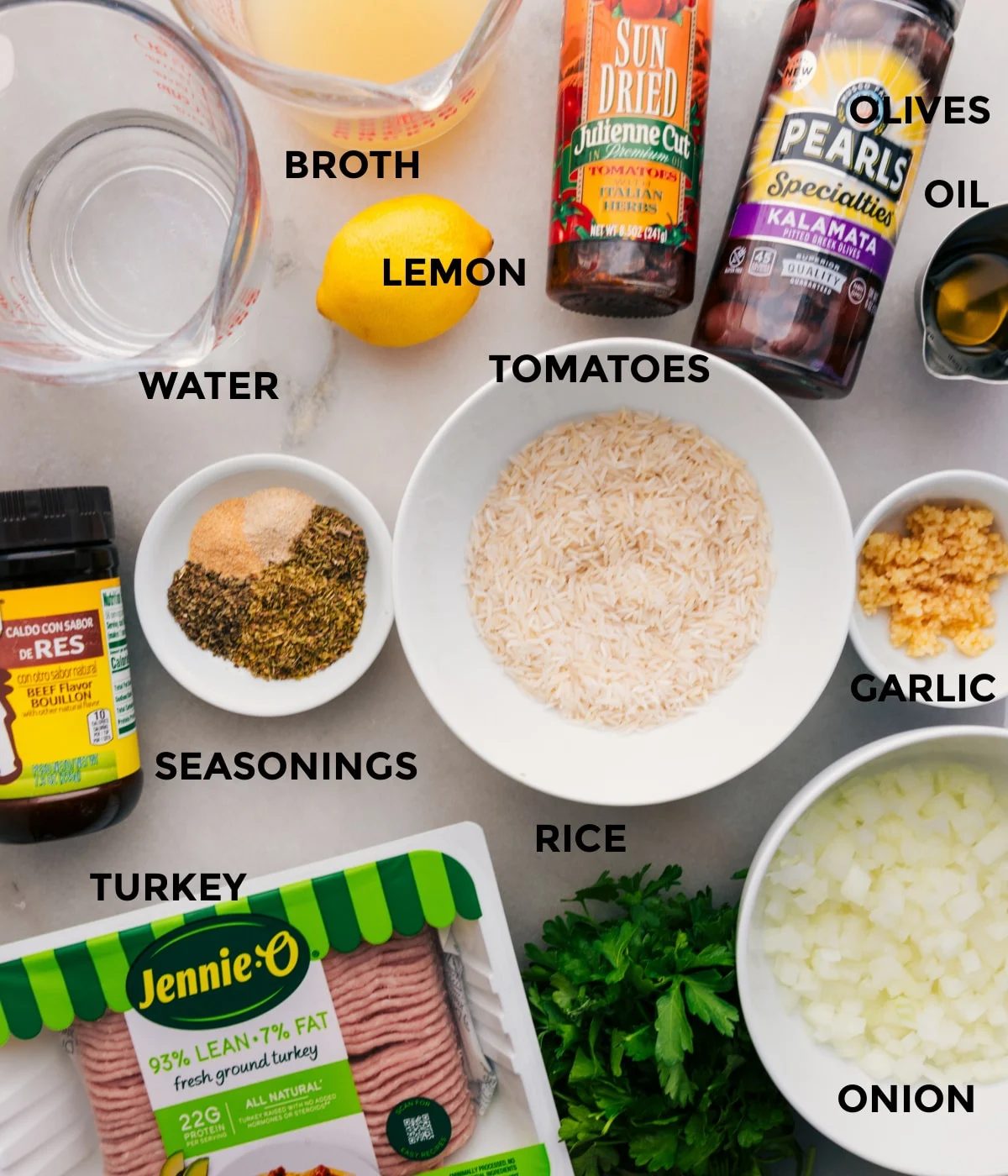 This recipe includes prepped ingredients like rice, veggies, meat, seasonings, olives, tomatoes, oil, broth, water, and lemons for straightforward assembly.