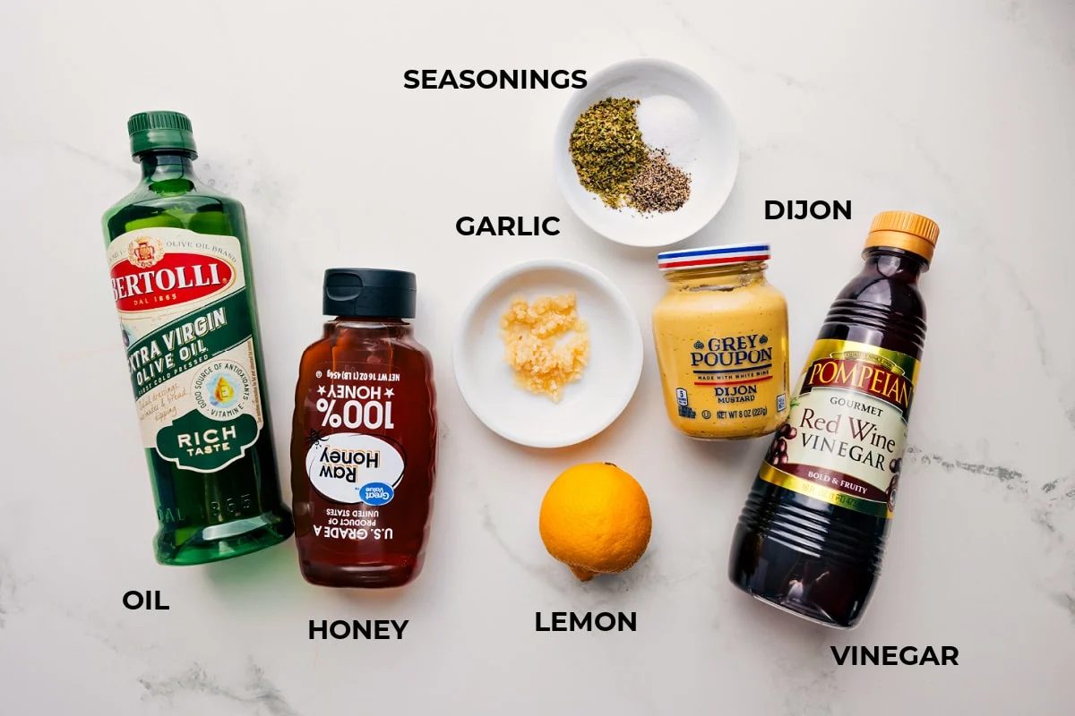 Greek quinoa salad ingredients prepped out for straightforward assembly including the oil, honey, seasonings, garlic, dijon, vinegar, and lemon.