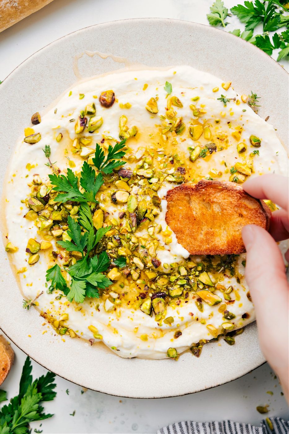 Greek recipes: Whipped feta recipe with pistachios on top with a piece of bread dipping in.