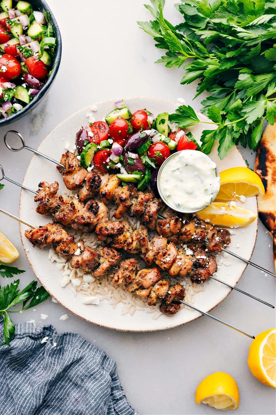 Greek Chicken Bowls on a plate with an straightforward greek salad, tzatziki dressing, all over rice.