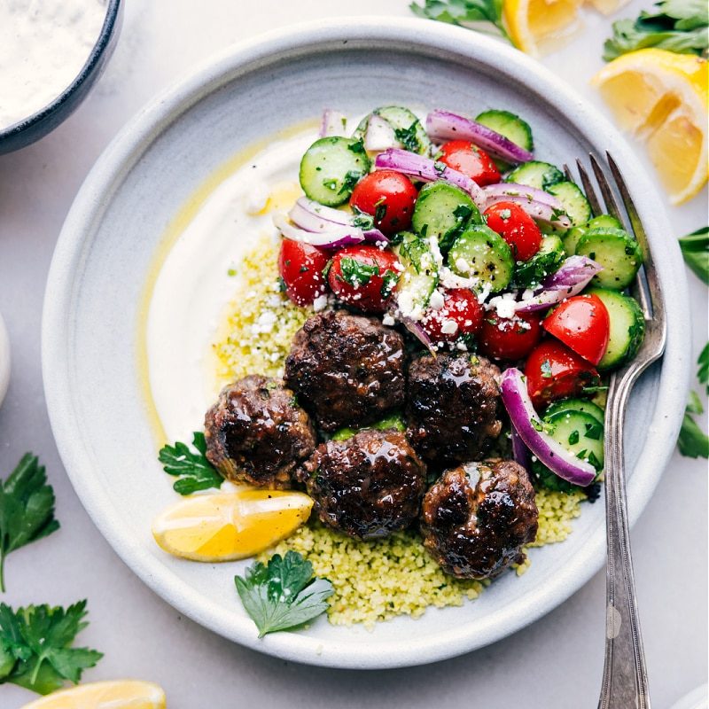 Meatball bowls filled with juicy meatballs, fluffy couscous, cucumber tomato salad, and a creamy lemon herb sauce.