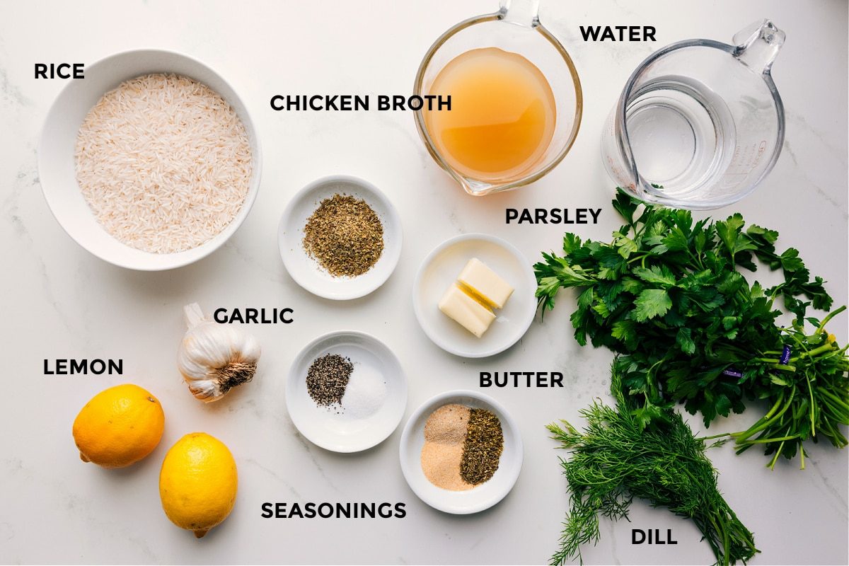 All the ingredients in this recipe prepped out for straightforward assembly including the rice, lemons, garlic, seasonings, butter, parsley, dill, chicken broth, and water.