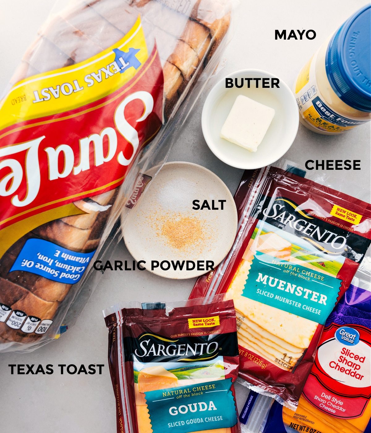 All the ingredients in this recipe prepped out for straightforward assembly including bread, cheddar, muenster, gouda, mayo, butter, and seasonings.