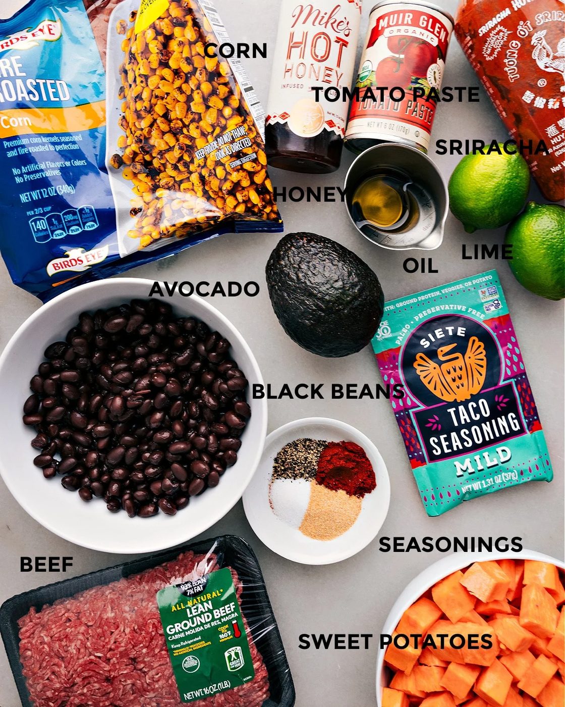 All the ingredients for this recipe are prepped and ready for straightforward assembly, including corn, hot honey, tomato paste, sriracha, lime, oil, avocado, seasonings, black beans, meat, and sweet potatoes.