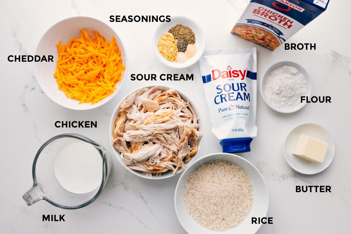 All the ingredients in this recipe prepped out for straightforward assembly including the milk, cheddar, chicken, seasonings, sour cream, rice, butter, flour, and broth.