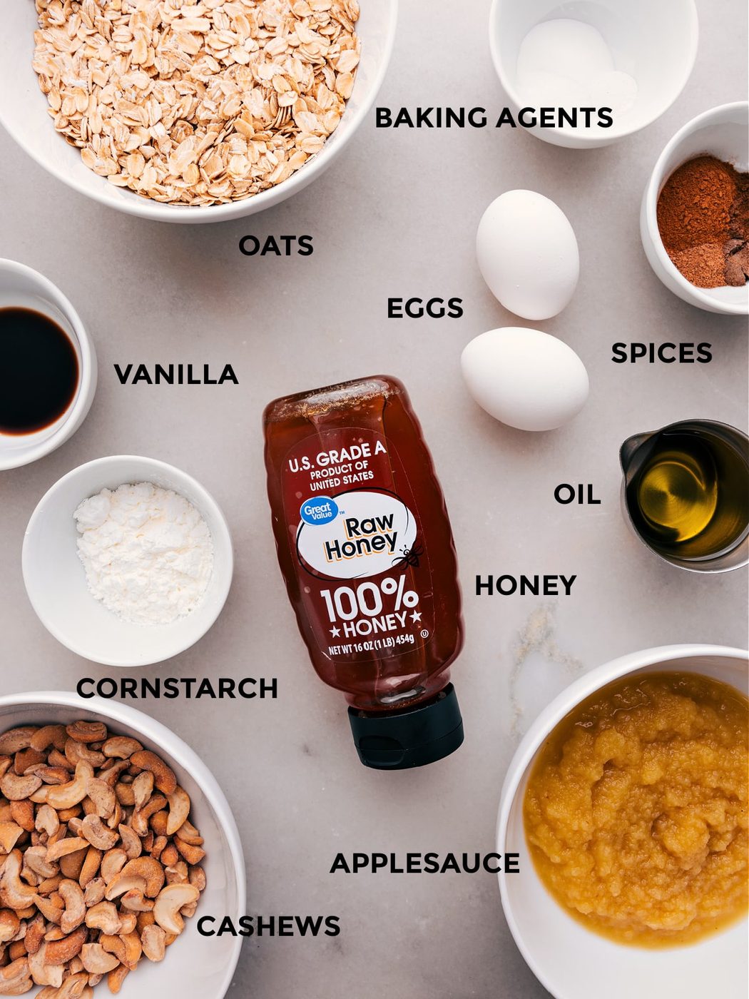 Prep all the ingredients for this recipe, including oats, baking agents, eggs, spices, oil, honey, vanilla, cornstarch, cashews, and applesauce, for straightforward assembly.