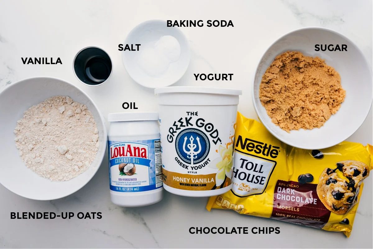 Ingredients prepped for straightforward assembly: blended oats, vanilla, salt, baking soda, oil, yogurt, chocolate chips, and sugar.