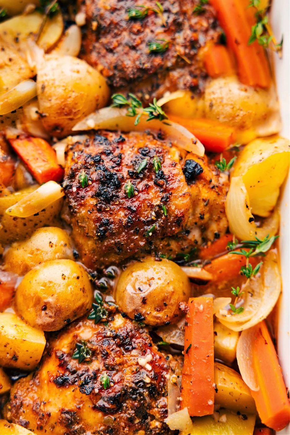 Roasted chicken and potatoes with colorful vegetables and fresh herbs.