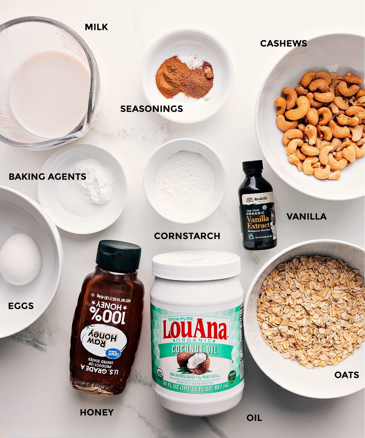 All the ingredients in this recipe prepped out for straightforward assembly including milk, seasonings, cashews, vanilla, cornstarch, baking agents, oats, coconut oil, honey, and eggs.