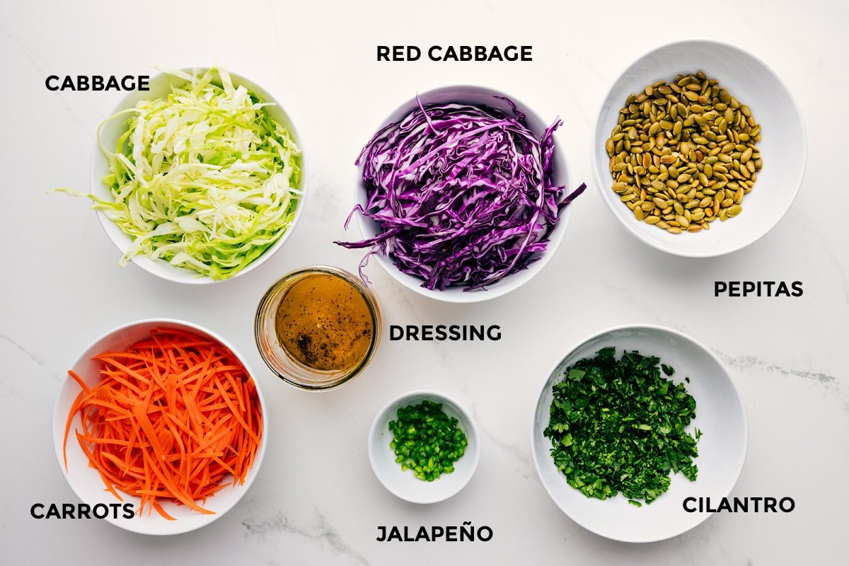 Ingredients prepped for straightforward assembly, including green and red cabbage, carrots, jalapeño, cilantro, pepitas, and dressing.
