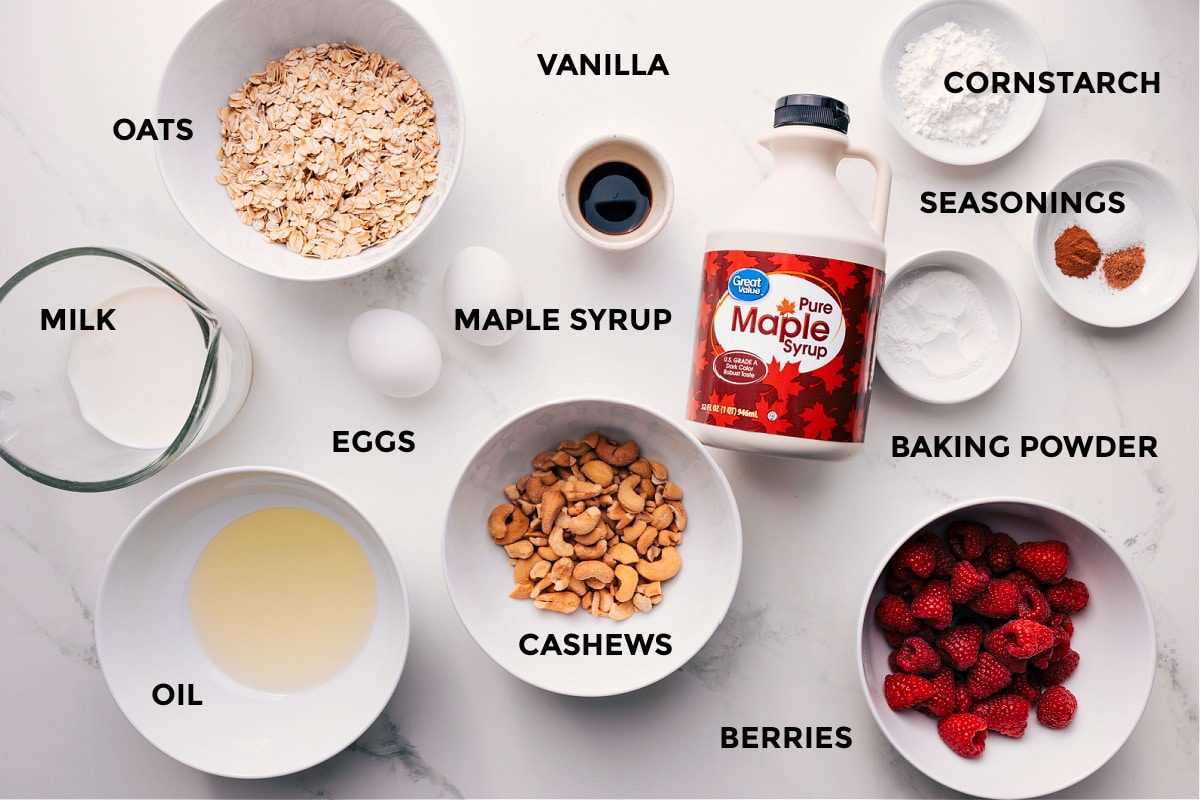 Ingredients prepped for straightforward assembly, including milk, oats, oil, eggs, cashews, vanilla, maple syrup, berries, baking powder, seasonings, and cornstarch.