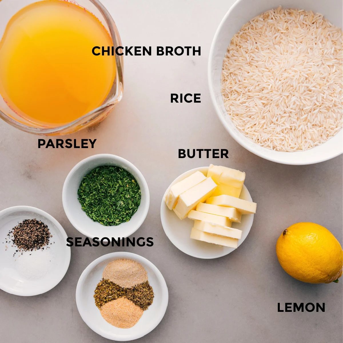All the ingredients for this recipe are prepped for straightforward assembly: chicken broth, seasonings, butter, rice, lemon, and fresh parsley.