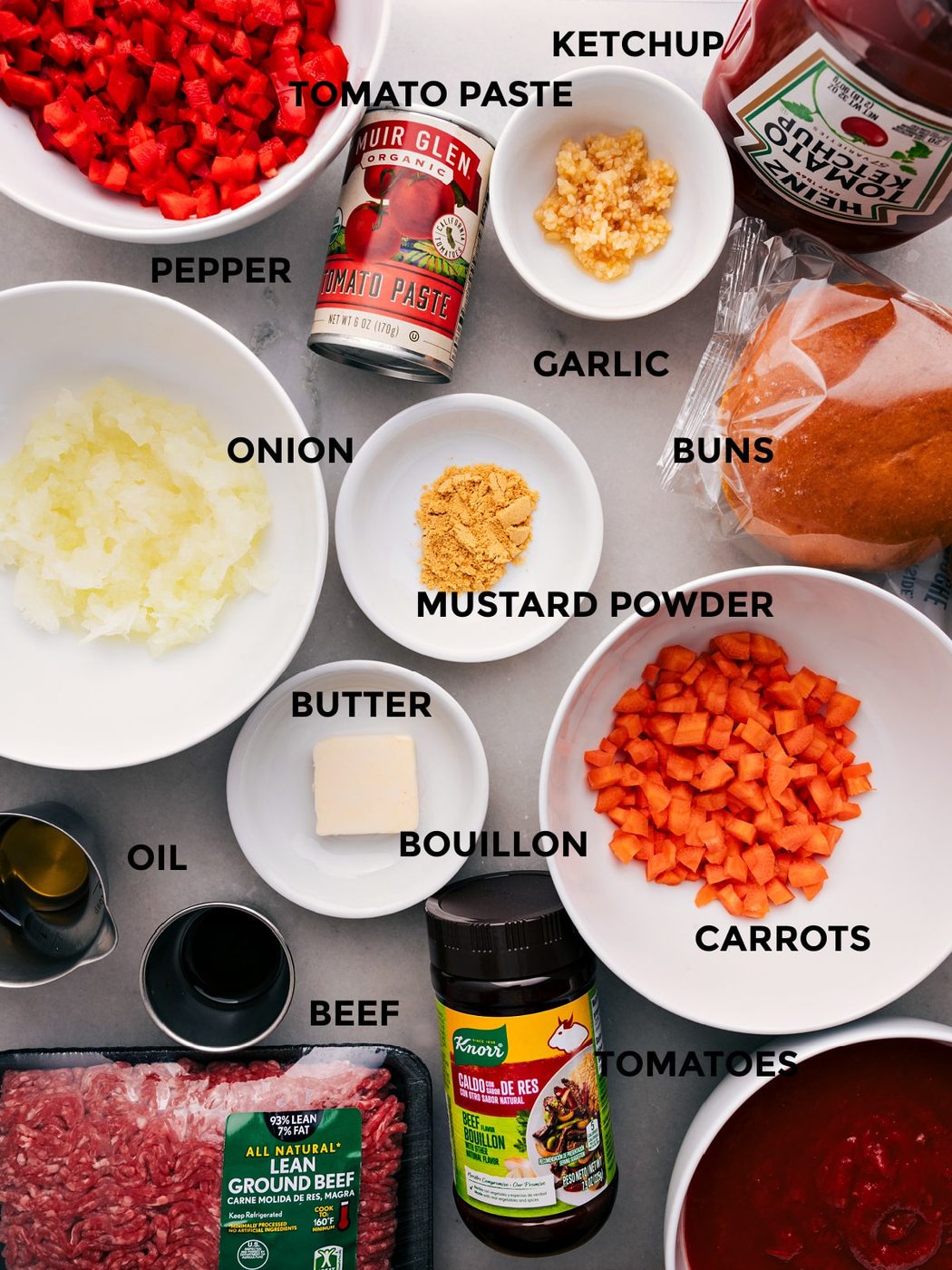 All the ingredients for this recipe—ketchup, pepper, tomato paste, buns, seasonings, onion, butter, bouillon, beef, and tomatoes—prepped and ready for straightforward assembly.