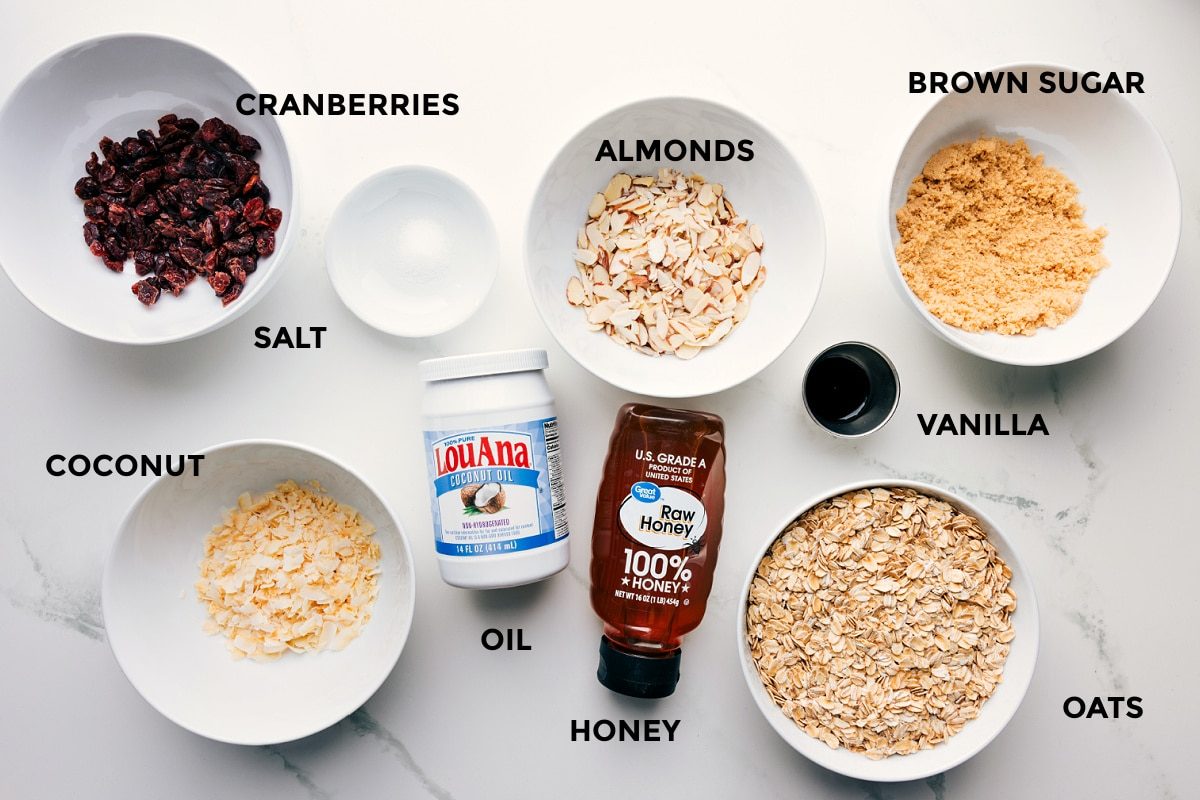 All the ingredients for Honey Almond Granola prepped and ready to assemble: cranberries, salt, almonds, brown sugar, vanilla, oats, honey, oil, and coconut.