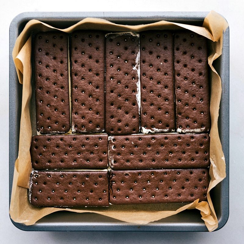 Ice cream sandwiches neatly lined up in a pan, forming the base layer of the frozen cake.