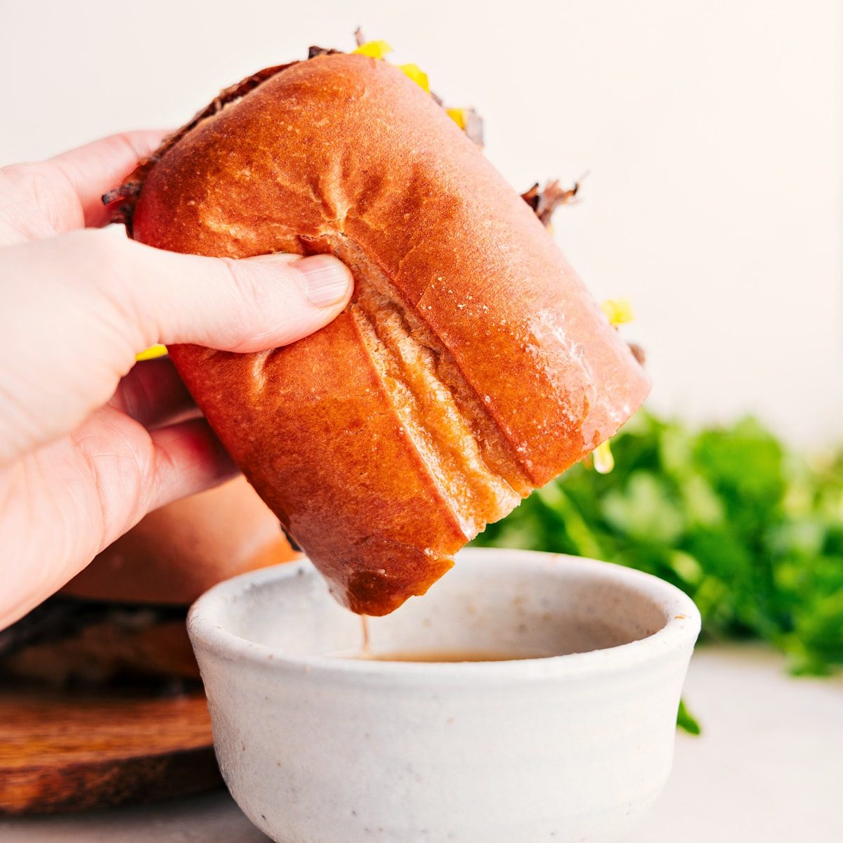 An Italian beef sandwich dipping into the broth from the slow cooker.