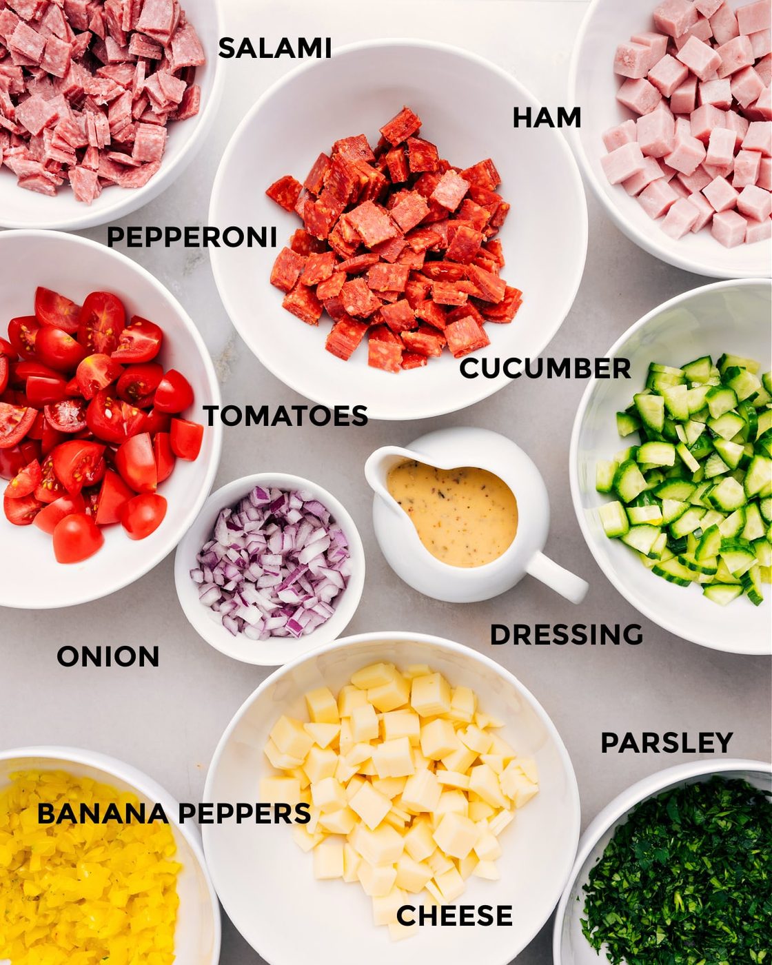 All the ingredients are prepped for straightforward assembly—meat, cucumber, tomatoes, onion, dressing, cheese, banana peppers, and parsley.