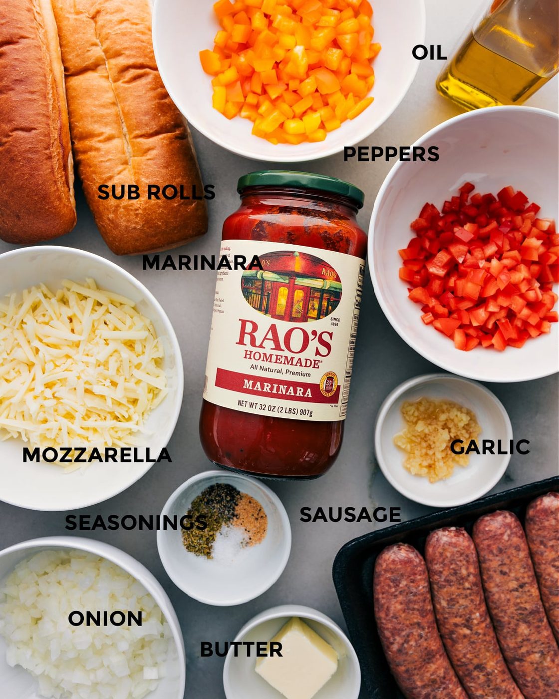 All the ingredients for this recipe are prepped and ready for straightforward assembly, including peppers, rolls, marinara, mozzarella, onion, seasonings, sausage, garlic, and butter.