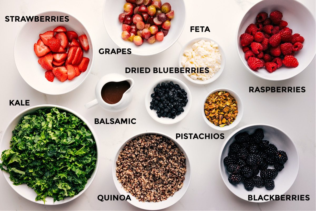 All the ingredients in this recipe prepped out for straightforward assembly including the kale, strawberries, grapes, feta, balsamic, quinoa, feta, dried blueberries, pistachios, blackberries, and raspberries.