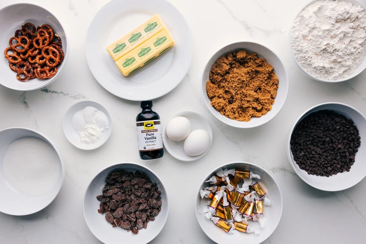 All the ingredients in this recipe prepped out for straightforward assembly including the pretzels, butter, sugar, baking agents, chocolate, caramels, brown sugar, and flour.