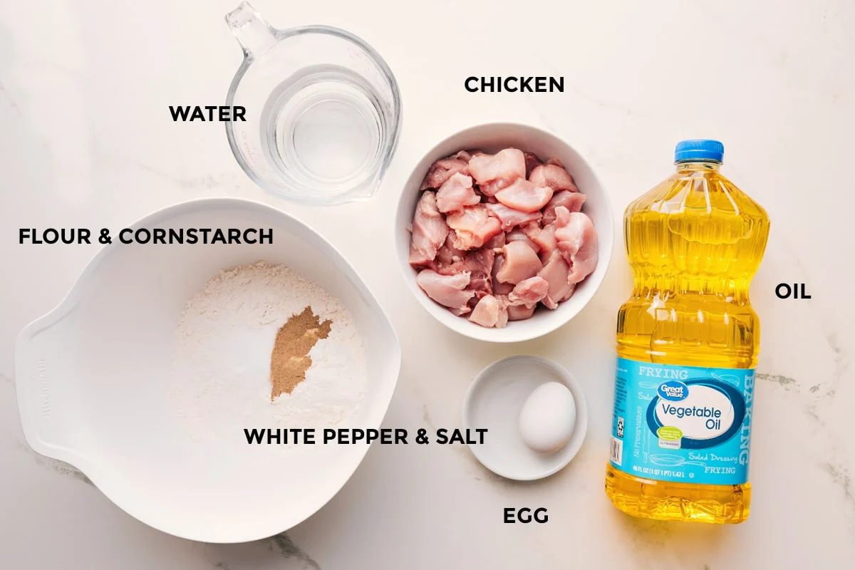 Korean chicken recipe ingredients prepped out for straightforward assembly including the flour, cornstarch, water, chicken, white pepper, salt, egg, and oil.