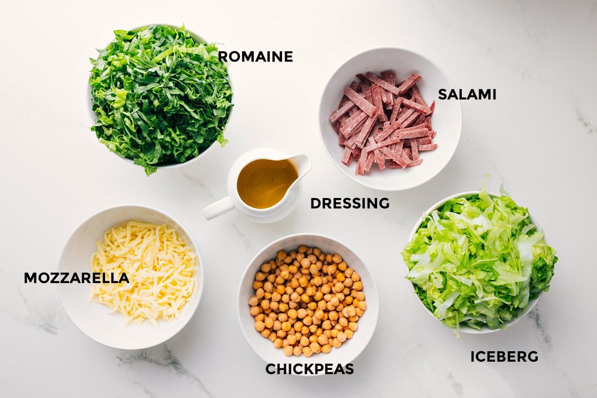 All the ingredients in this recipe prepped out for straightforward assembly including the romaine, mozzarella, salami, iceberg, chickpeas, and dressing.