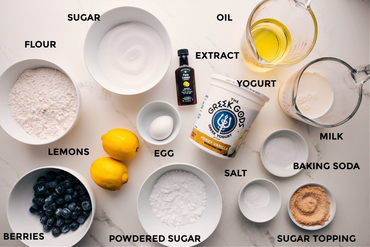 All the ingredients in this recipe prepped out for straightforward assembly including the flour, berries, lemons, powdered sugar, egg, sugar, extract, oil, milk, baking soda, salt, and yogurt.
