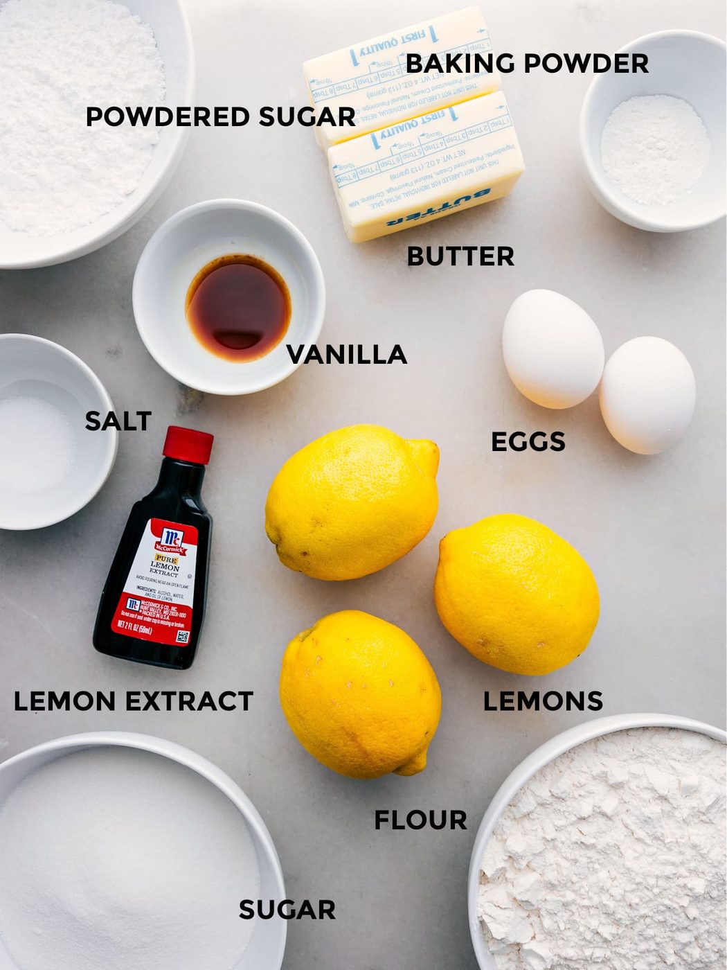 All the ingredients in this recipe prepped out for straightforward assembly including the powdered sugar, baking powder, butter, eggs, vanilla, salt, lemons, lemon extract, flour, and sugar.
