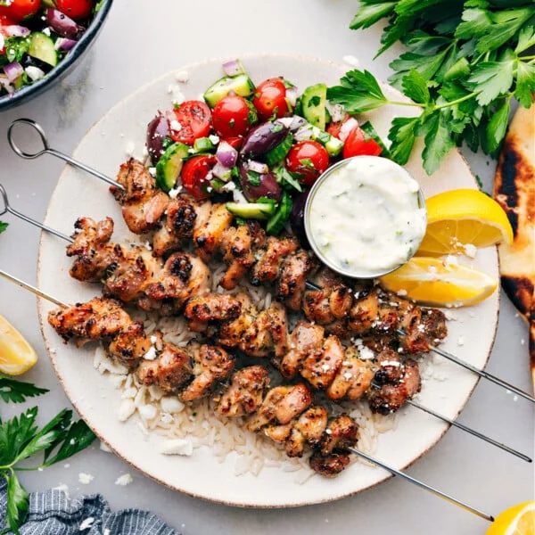 Greek Chicken Bowls on a plate with an straightforward greek salad, tzatziki dressing, all over rice.