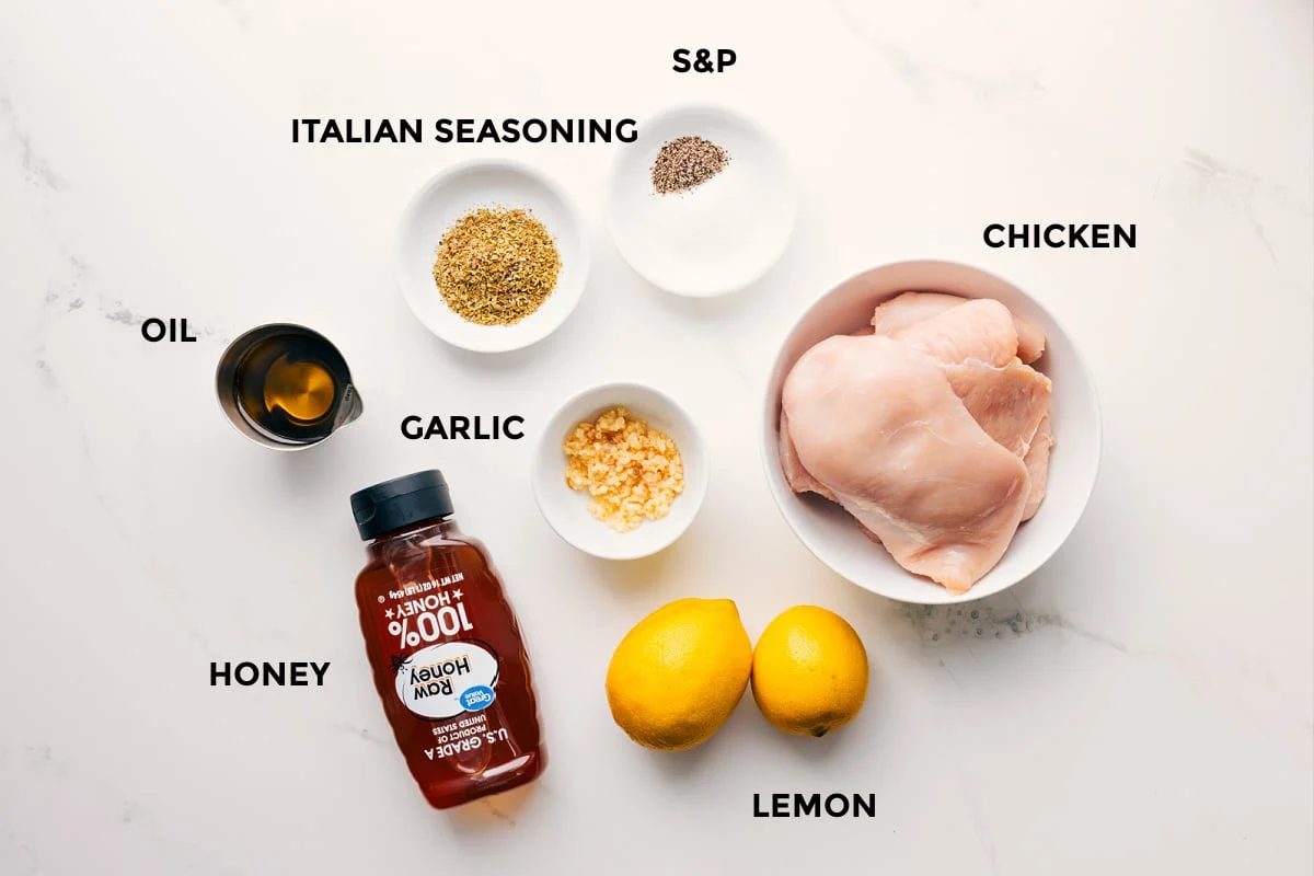 The ingredients in this recipe prepped out for straightforward assembly including the oil, honey, seasonings, garlic, chicken, and lemons.