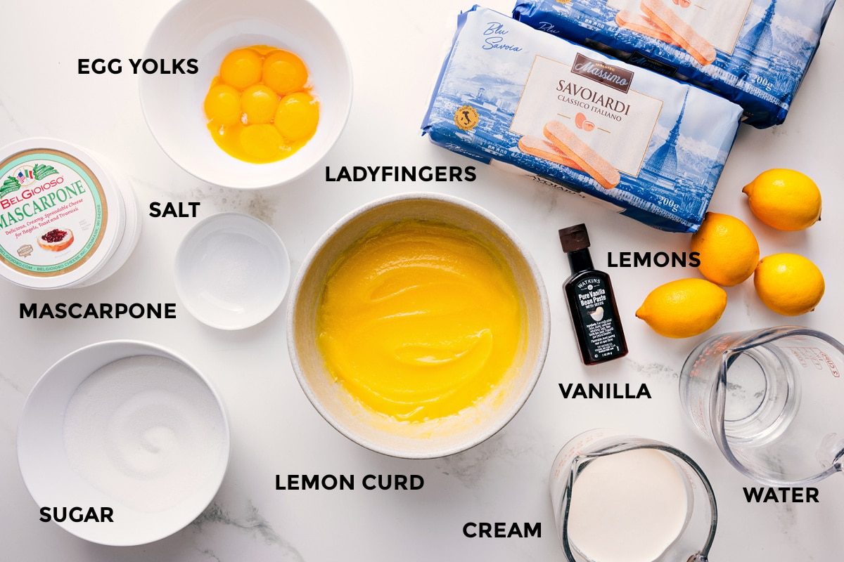 All the ingredients in this recipe prepped out for straightforward assembly including the egg yolks, salt, mascarpone, sugar, lemon curd, cream, water, lemons, vanilla, and ladyfingers.