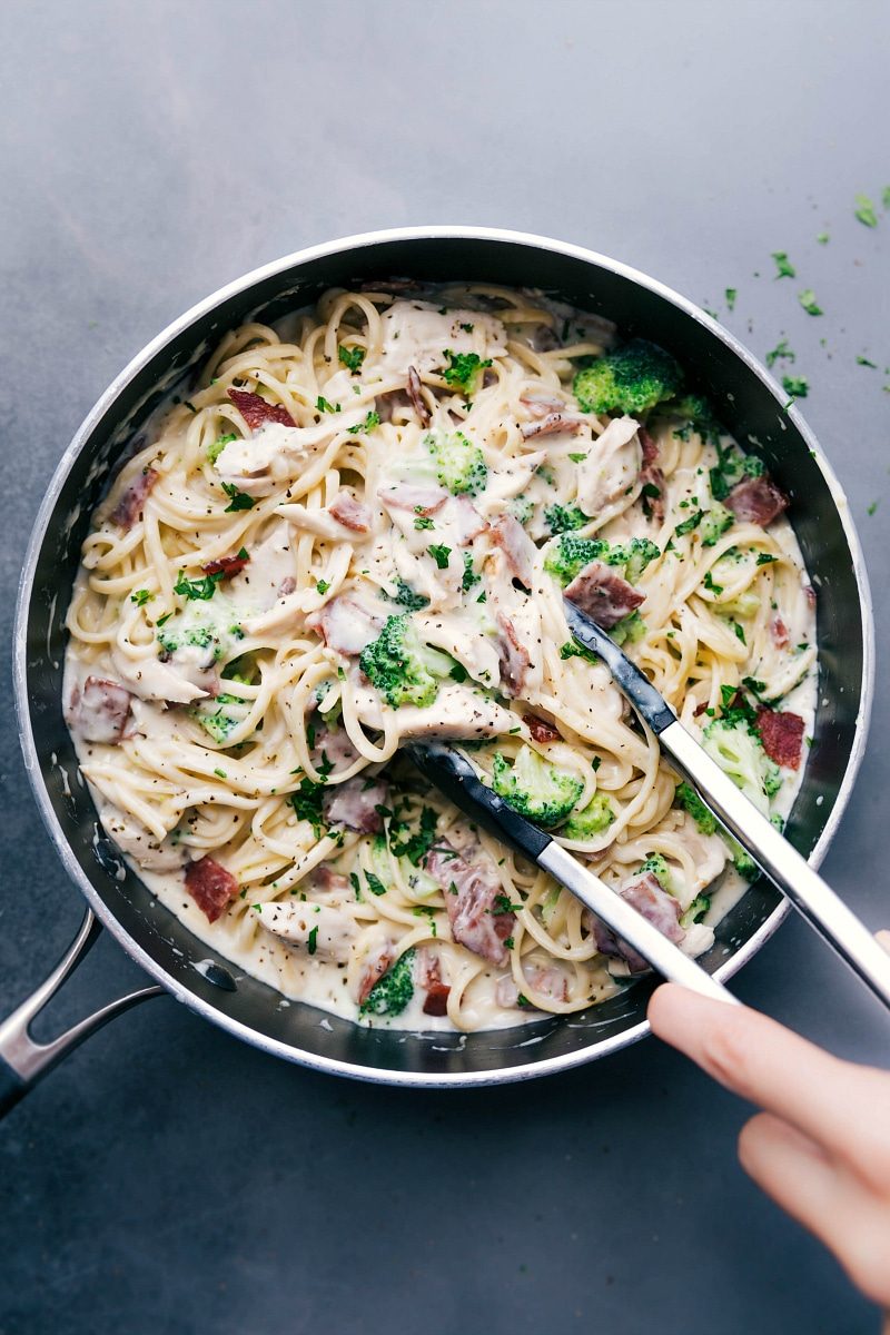 Chicken broccoli alfredo with tongs scooping up a creamy and satisfying bite, ready to be enjoyed.