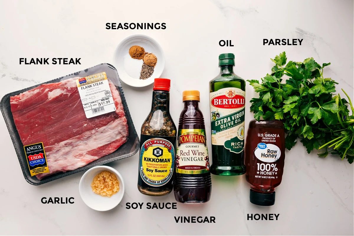 All the ingredients in this recipe prepped out for straightforward assembly including the steak, garlic, soy sauce, vinegar, honey, parsley, oil, and seasonings.