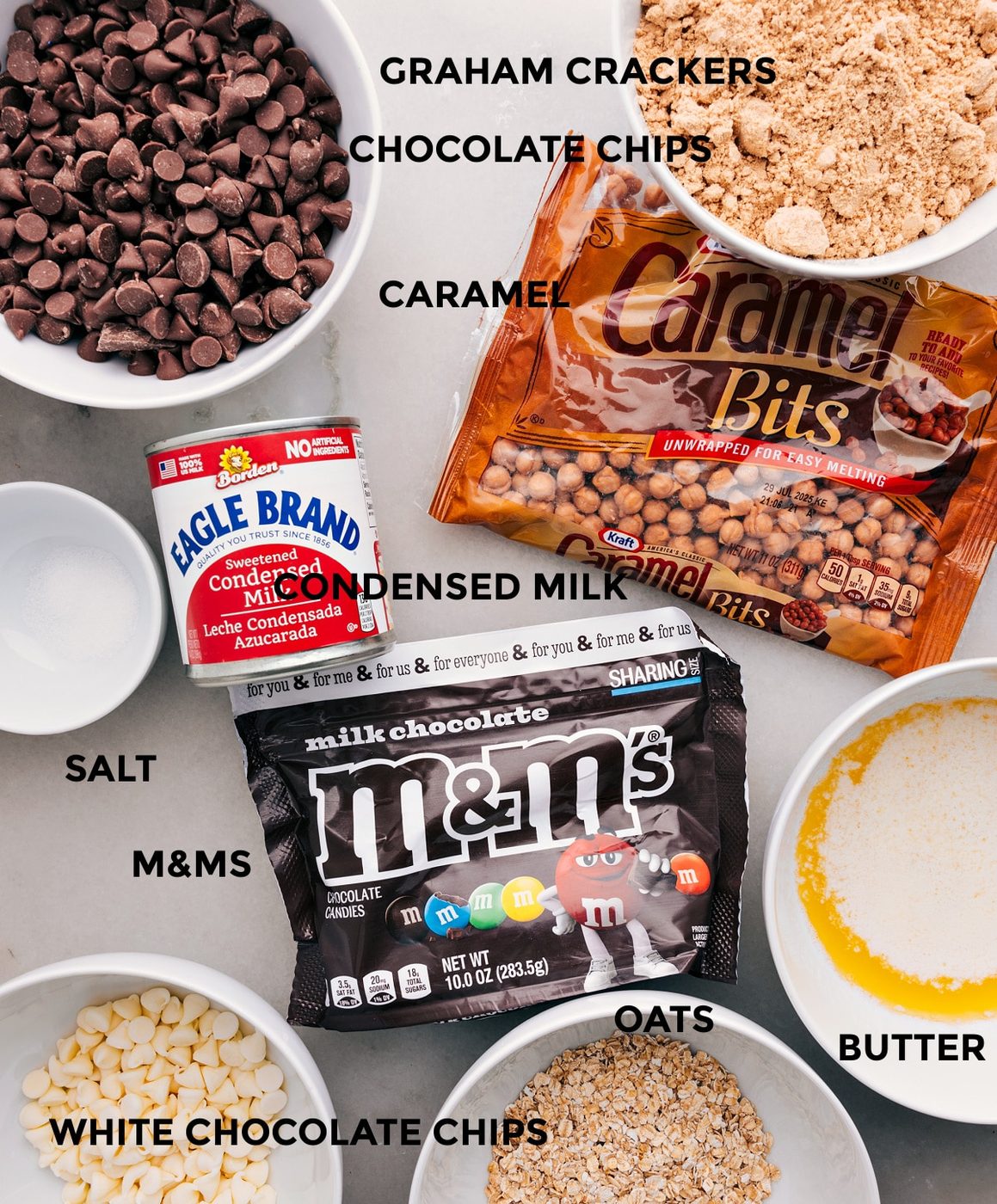 All the ingredients are prepped and ready for straightforward assembly—graham crackers, caramel bits, condensed milk, chocolate chips, M&Ms, butter, oats, and salt.