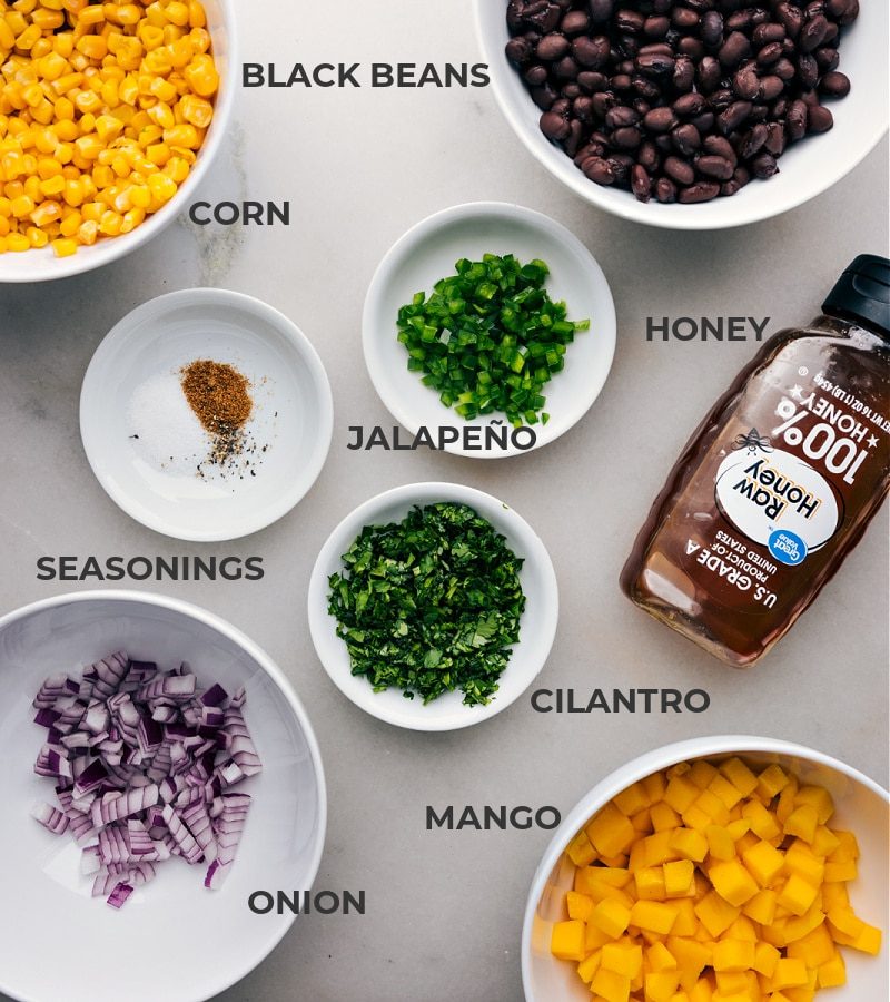 Ingredients in this recipe prepped and ready to go, including beans, corn, honey, jalapeño, seasonings, onion, and fruit.