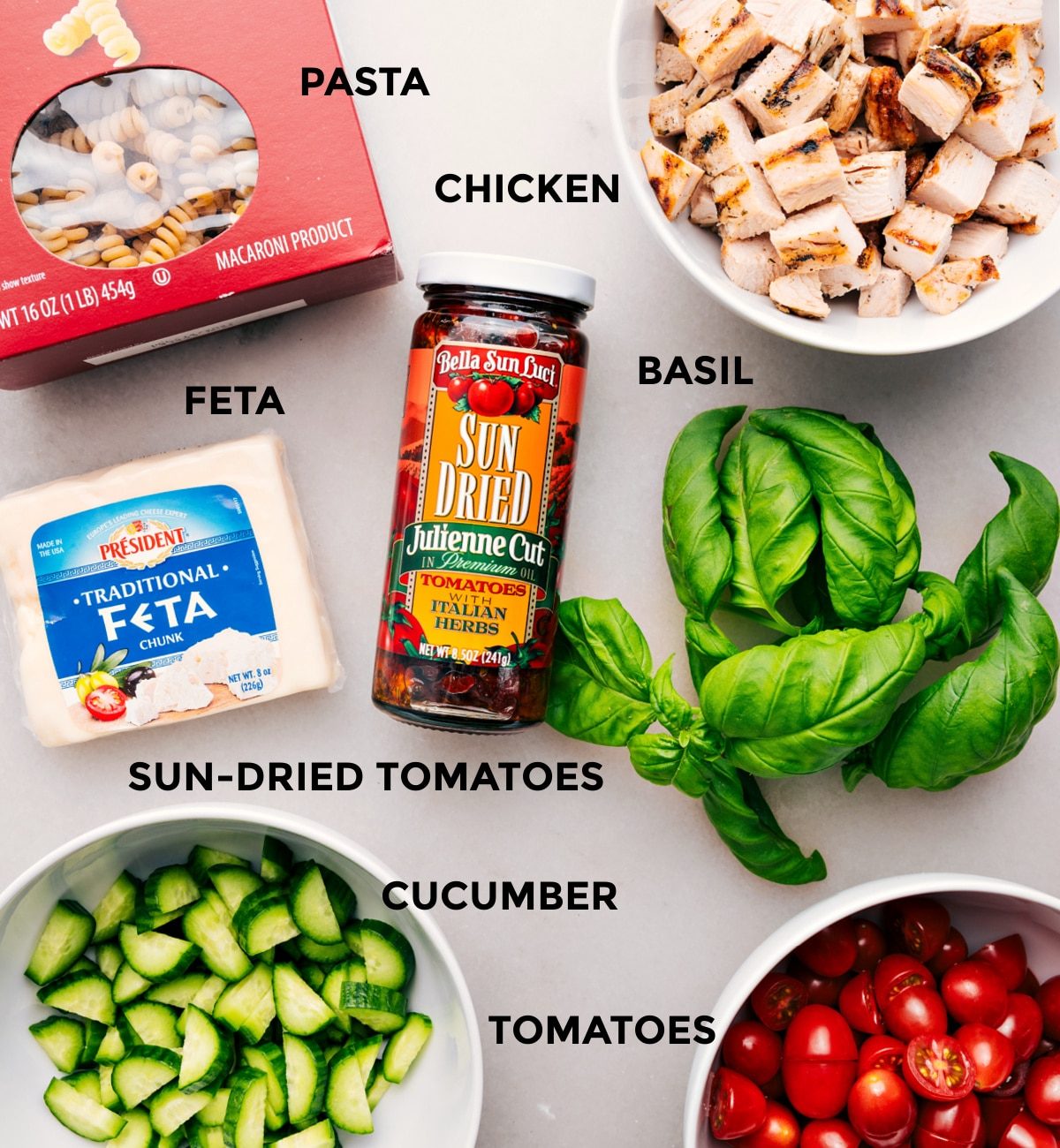 Everything’s prepped for straightforward assembly—pasta, chicken, basil, feta, sun-dried tomatoes, cucumber, and tomatoes.