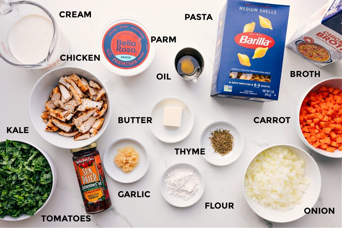 All the ingredients prepped and ready to assemble, including cream, chicken, kale, tomatoes, garlic, Parmesan, oil, butter, flour, thyme, pasta, carrot, onion, and broth.