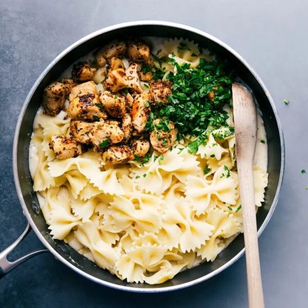 Pasta, chicken, and fresh parsley over the alfredo sauce, about to be mixed together to create a satisfying meal.