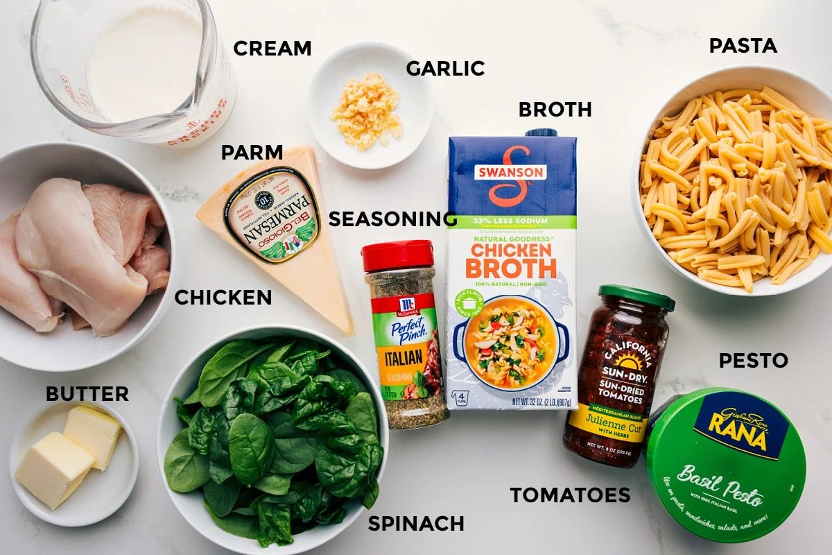 All the ingredients prepped for straightforward assembly: pasta, pesto, tomatoes, broth, garlic, cream, Parmesan, seasonings, butter, spinach, and chicken.