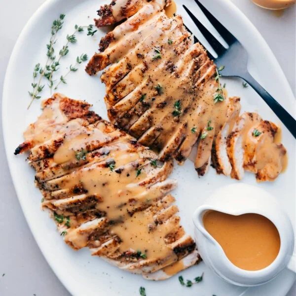 Sliced turkey breast cooked in a slow cooker, served on a plate topped with gravy and garnished with fresh herbs.