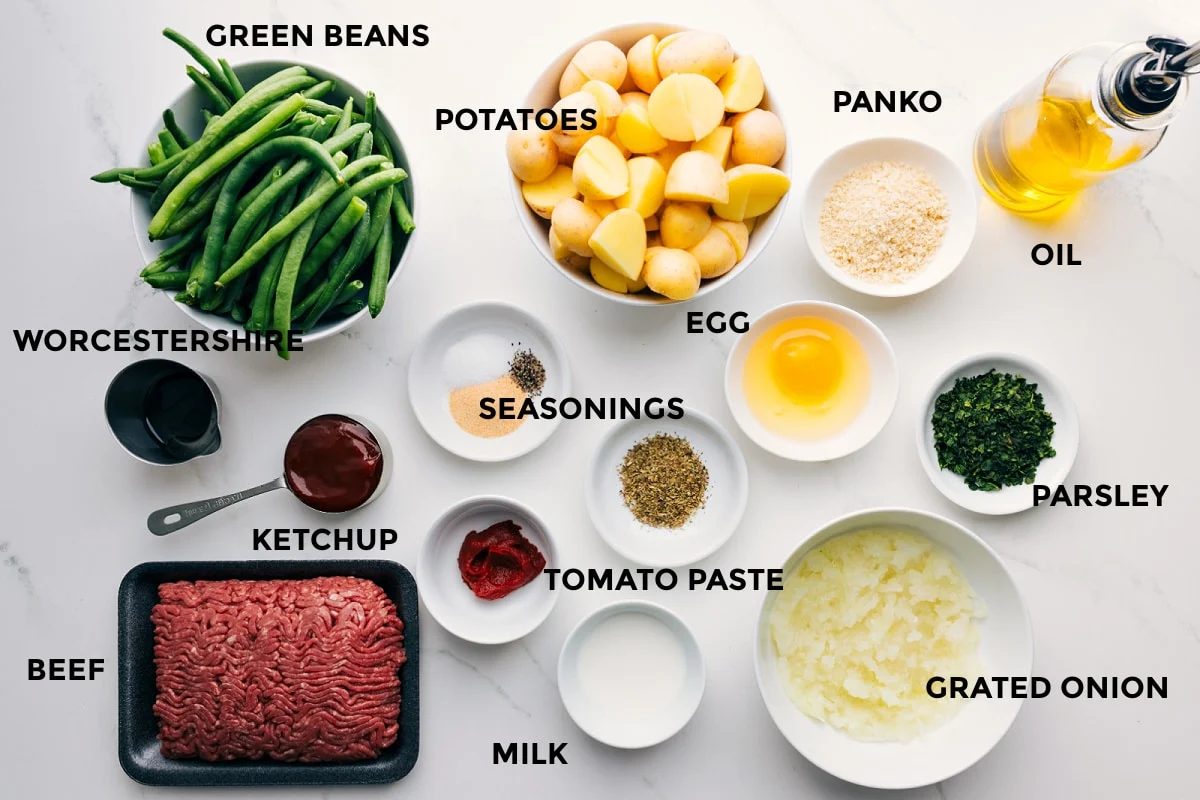 All the ingredients for this recipe prepped and ready for straightforward assembly including green beans, Worcestershire sauce, ketchup, ground beef, milk, tomato paste, seasonings, grated onion, parsley, egg, potatoes, panko, and oil.