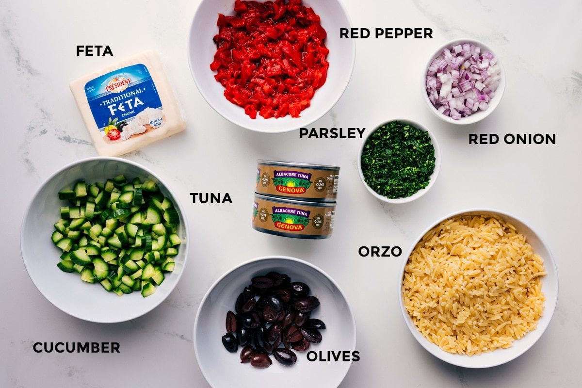 All the ingredients for Mediterranean Tuna Salad prepped for straightforward assembly, including feta, red pepper, red onion, parsley, orzo, olives, tuna, and cucumber.