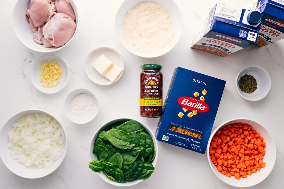 All the ingredients in this recipe prepped out for straightforward assembly including the chicken, onions, spinach, carrots, sun-dried tomatoes, pasta, seasonings, broth, butter.
