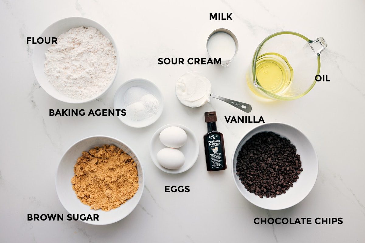 All the ingredients in this recipe prepped out for straightforward assembly including the flour, baking agents, brown sugar, eggs, sour cream, milk, vanilla, chocolate chips, and oil.