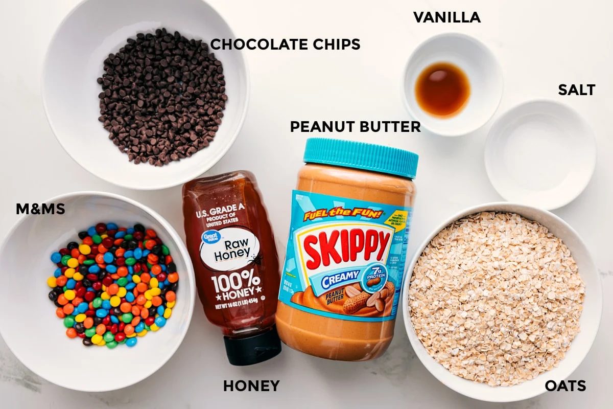 All the ingredients in this recipe prepped out for straightforward assembly including m&ms, chocolate chips, honey, peanut butter, vanilla, salt, and oats.