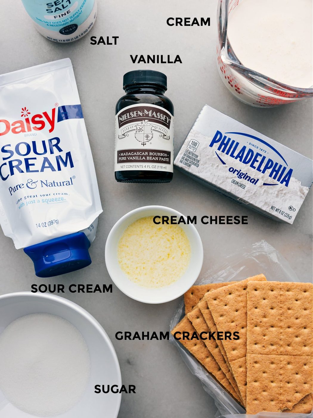 Ingredients for this recipe prepped out for straightforward assembly including the sour cream, cream cheese, butter, graham crackers, sugar, cream, vanilla, and salt.