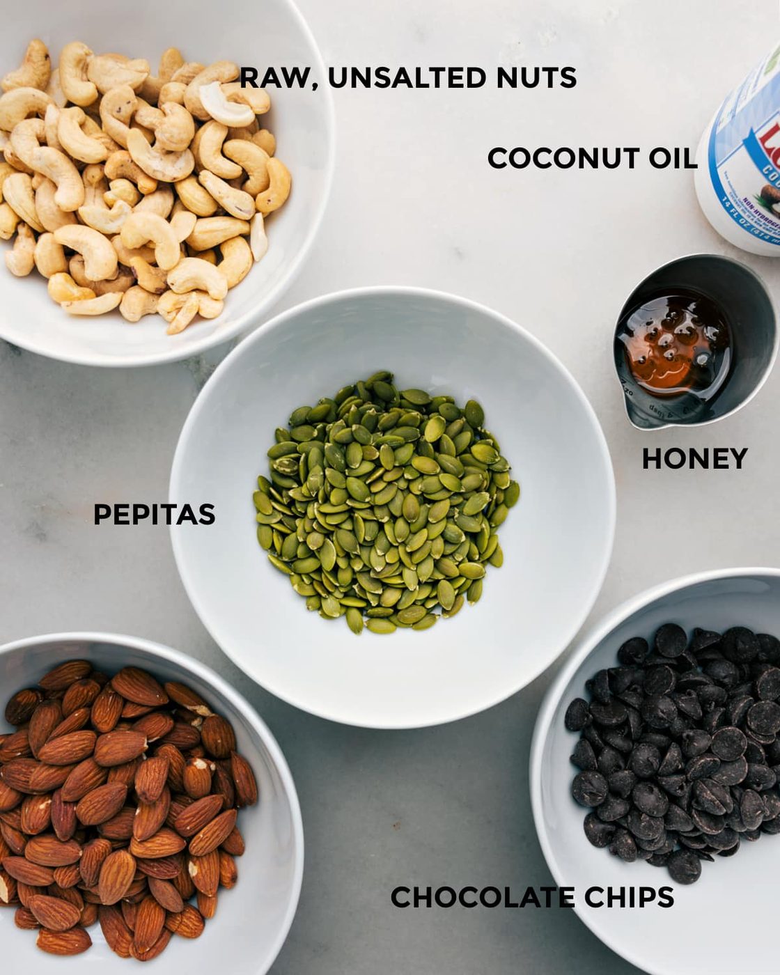 All the ingredients in this recipe like nuts, coconut oil, pepitas, honey, and chocolate chips prepped out for straightforward assembly.