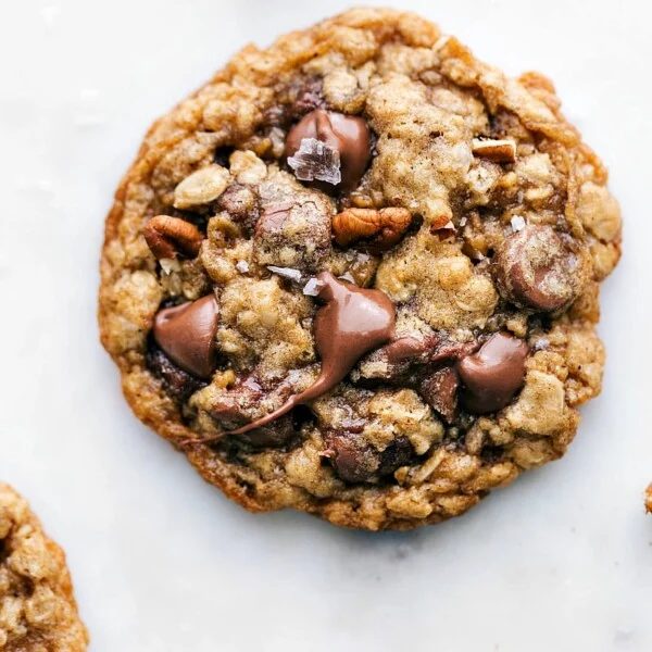 Freshly baked and satisfying oatmeal pecan cookie with melted chocolate chips on top, a sprinkle of fresh sea salt, and baked pecans.